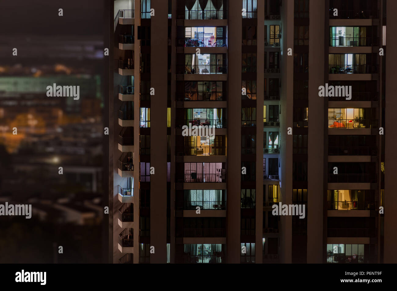 Background with night life in big city - modern high-rise building with windows of cozy apartments in which light shines, people doing routine things. Stock Photo