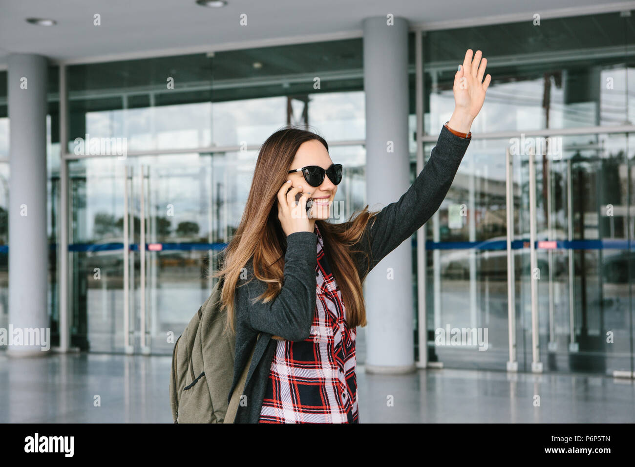 Young beautiful tourist girl at the airport or near the shopping center or the station calls a taxi or talking on a cell phone or talking to friends using a mobile phone Stock Photo