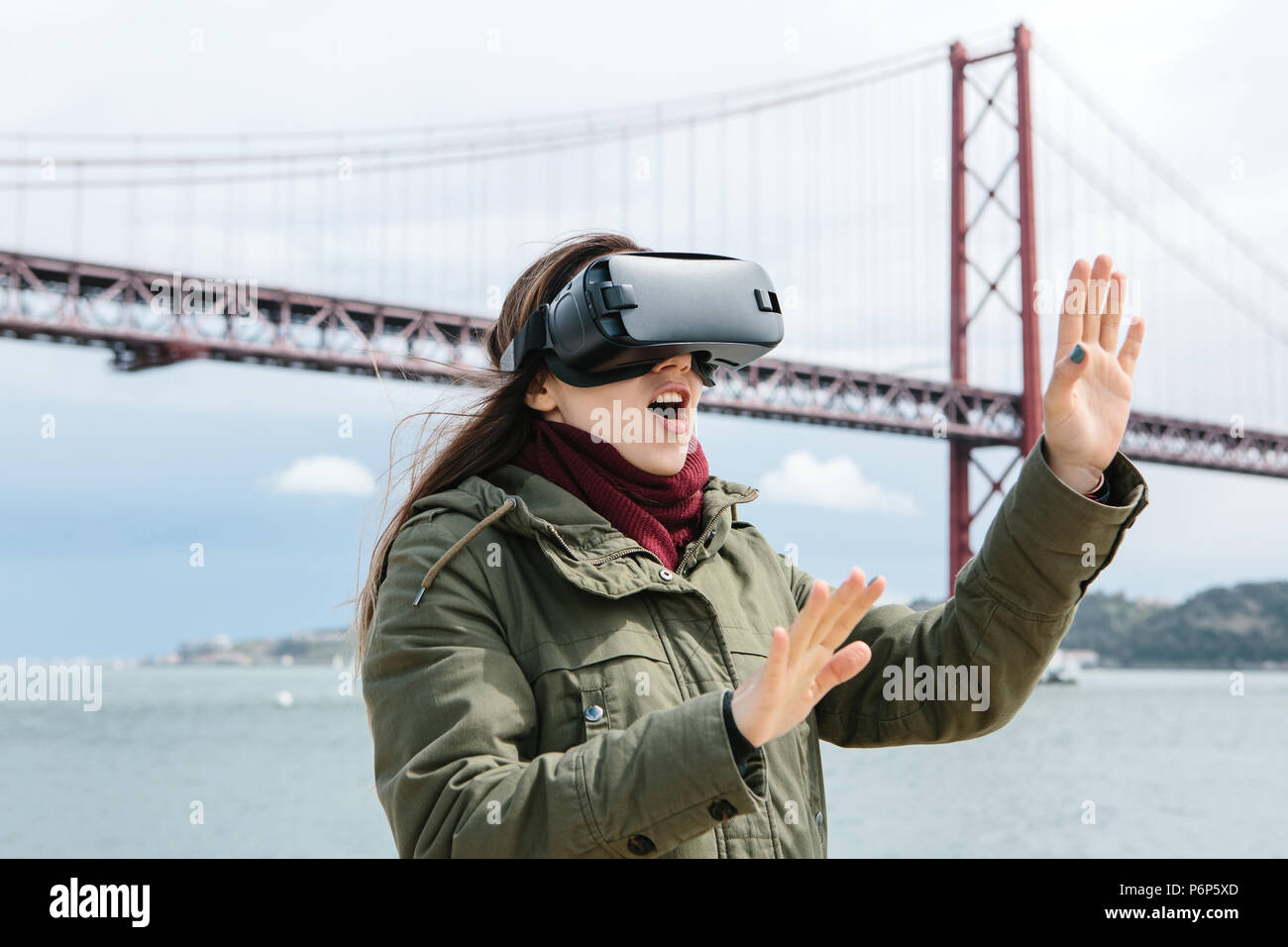 Young beautiful girl wearing virtual reality glasses. 25th of April bridge in Lisbon in the background. The concept of modern technologies and their use in everyday life Stock Photo