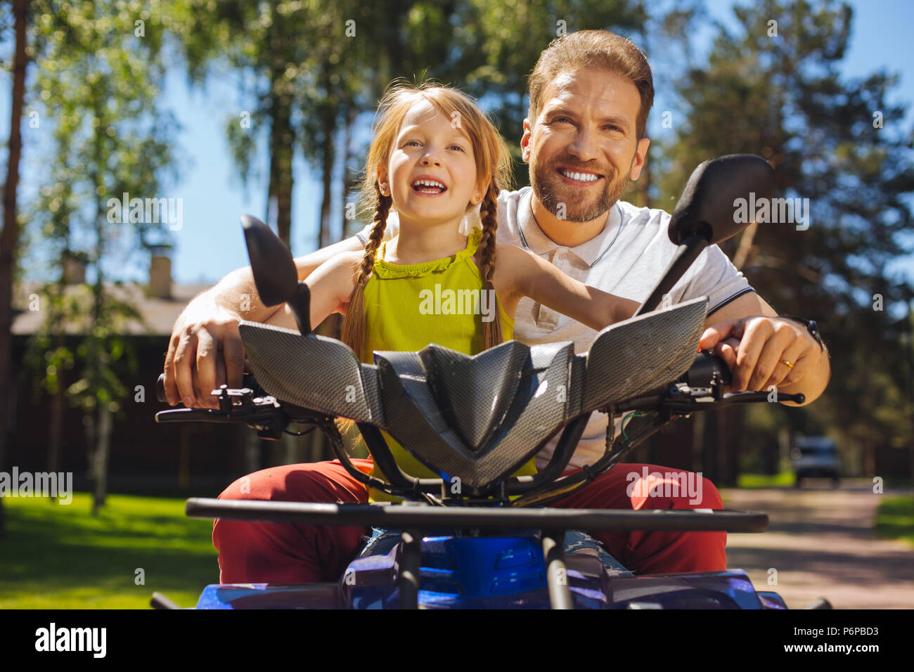 Smiling girl driving ATV with her daddy Stock Photo