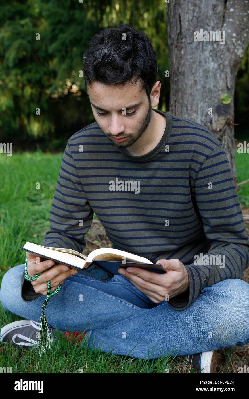 Young man reading the Kuran in a park. France. Stock Photo