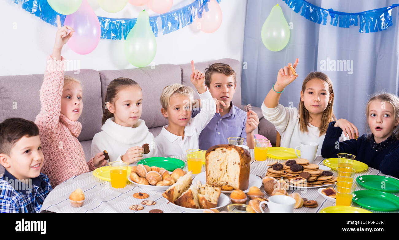 Cheerful children having dinner to celebrate friend’s birthday Stock