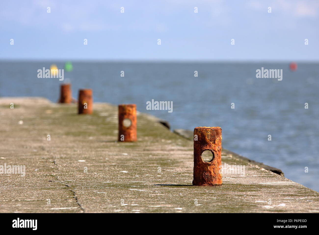 Empty beton shore with few corroded small poles with wholes inside, one by one, lake (sea), horizon, blue sky Stock Photo