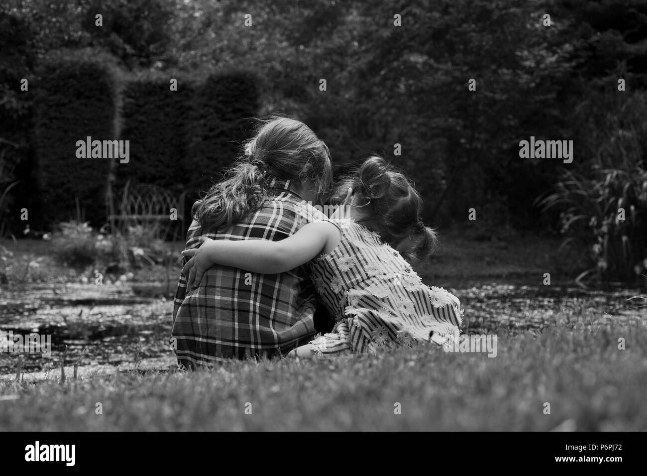 Little girl hugging her friend by a pond. Stock Photo