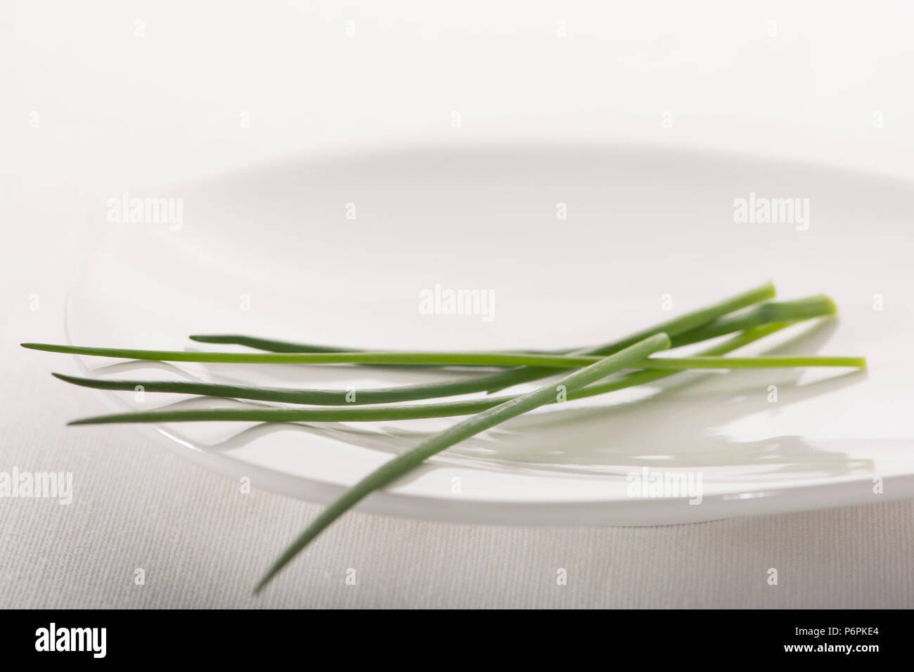 Close up of some scapes of  the common green herb chives, on a white plate against a white background Stock Photo