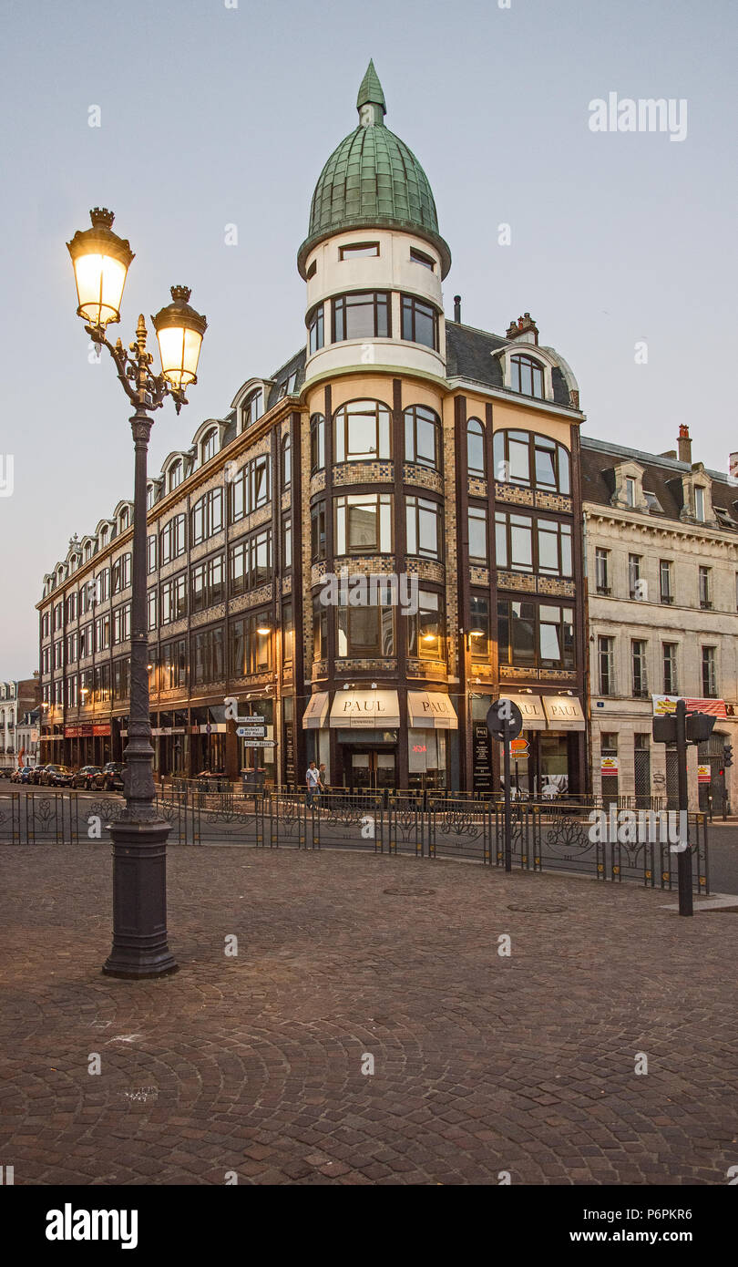 Stylish buildigns and shops with lights and illuminated lamp stand at  corner of Rue de la Sellerie and Rue d'Isle St Quentin, Aisne, France Stock Photo