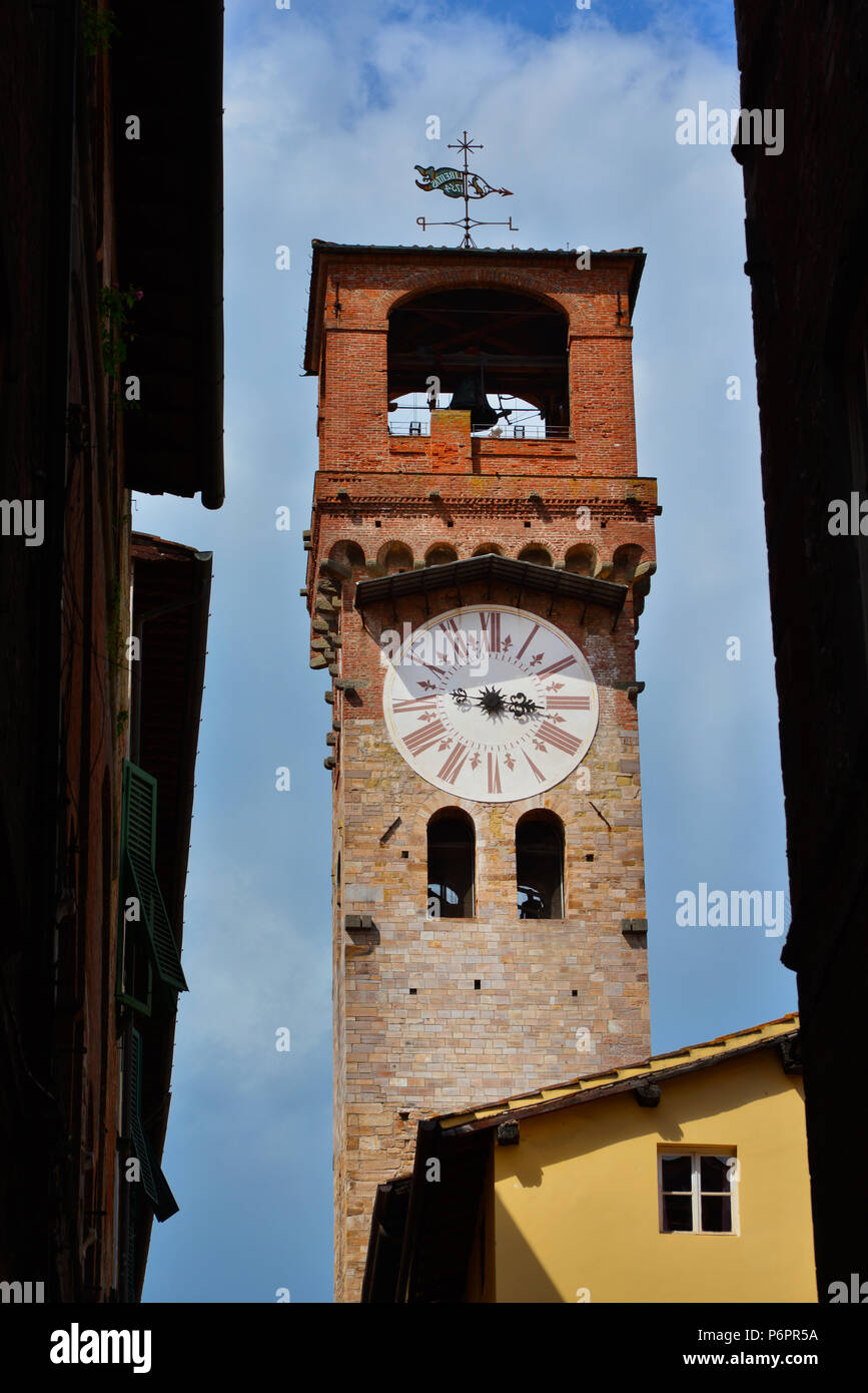Lucca medieval 'Torre delle Ore' (Clock Tower), seen from a narrow street in city historic center with cloudy sky Stock Photo