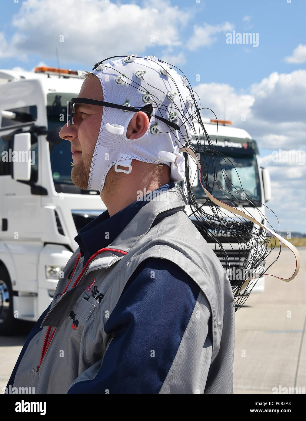 02 July 2018, Germany, Selchow: Truck driver Andy Kipping wearing a control system with which - with the aid of electroencephalography (EEG) and eye tracking - the effects of semi-autonomous driving on the driver's wakefulness and role understanding can be tracked, during a demonstration of platooning in autonomous driving in the unused south strip of Schoenefeld Airport. Platooning is convoy driving with very small distances between trucks through the aid of a technological driving system. DB Schenker, MAN Truck & Bus and the Fresenius University of Applied Sciences are for the first time tes Stock Photo