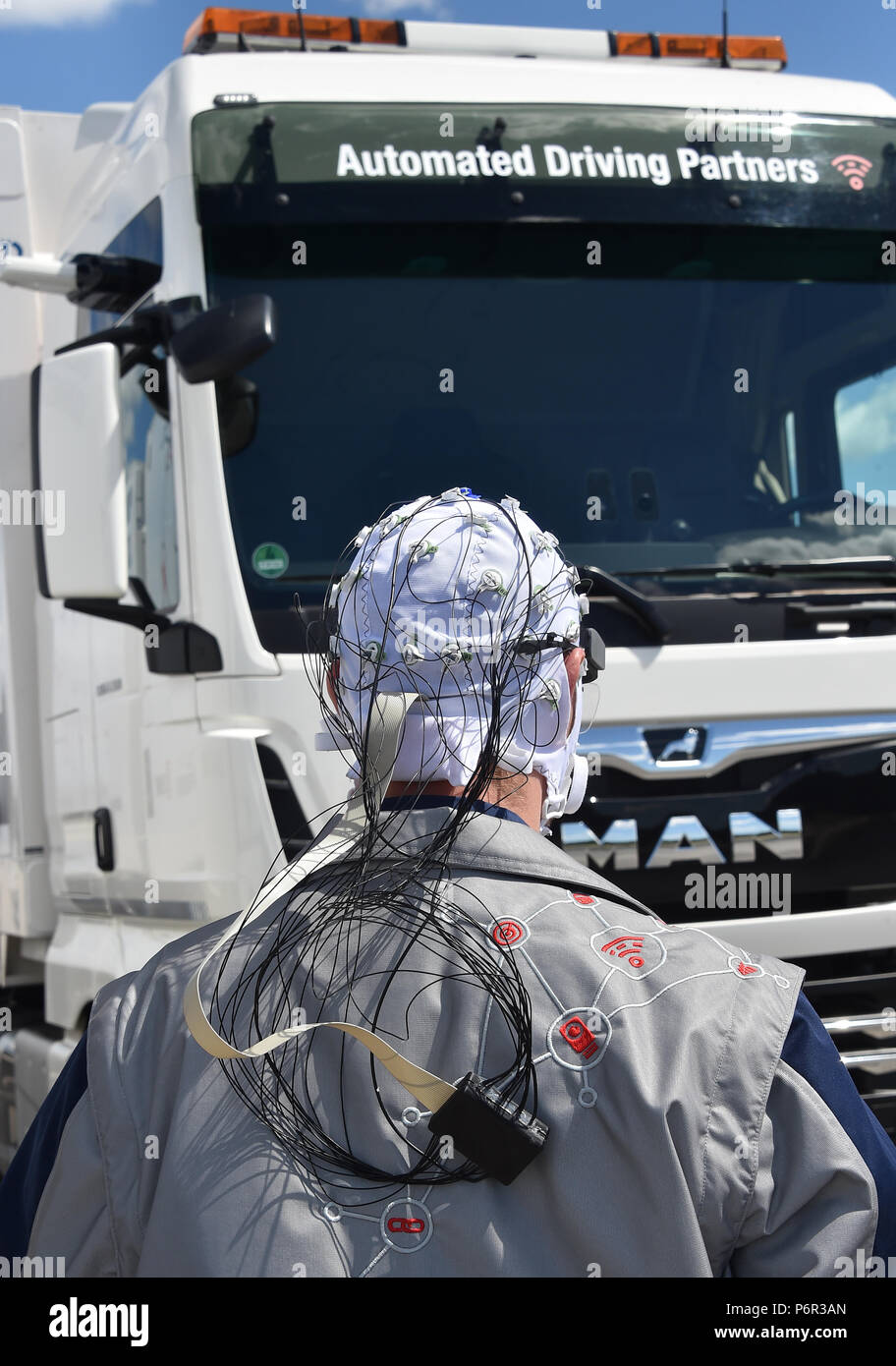 02 July 2018, Germany, Selchow: Truck driver Andy Kipping wearing a control system with which - with the aid of electroencephalography (EEG) and eye tracking - the effects of semi-autonomous driving on the driver's wakefulness and role understanding can be tracked, during a demonstration of platooning in autonomous driving in the unused south strip of Schoenefeld Airport. Platooning is convoy driving with very small distances between trucks through the aid of a technological driving system. DB Schenker, MAN Truck & Bus and the Fresenius University of Applied Sciences are for the first time tes Stock Photo