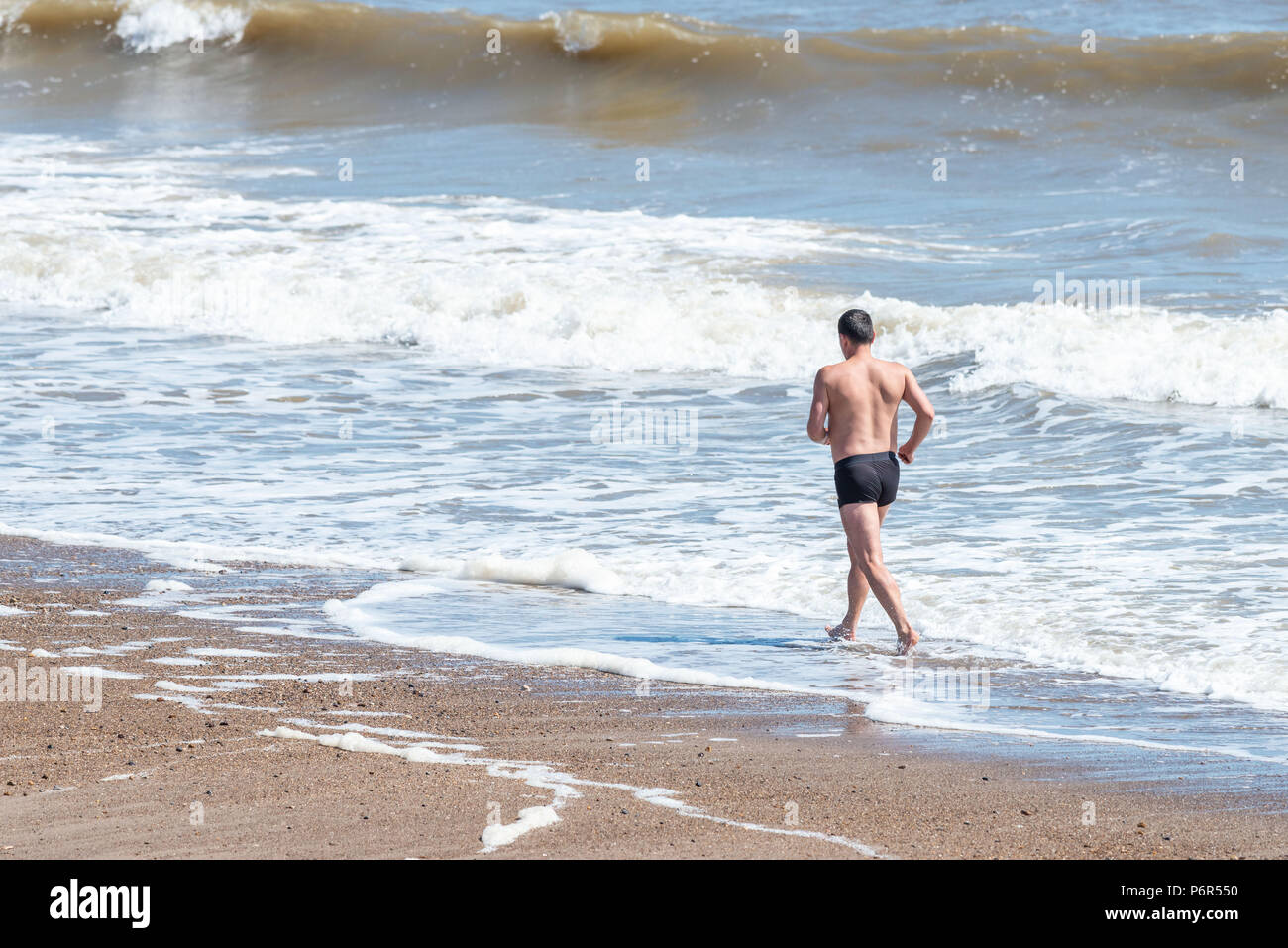 Skegness, UK, 2nd July 2018. A man jogging on the beach uses the incoming waves to keep himself cool, as the continued hot weather keeps temperatures in the UK at a high. Credit: Steven Booth/Alamy Live News. Stock Photo