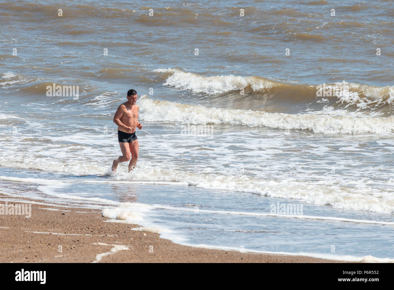 Skegness, UK, 2nd July 2018. A man jogging on the beach uses the incoming waves to keep himself cool, as the continued hot weather keeps temperatures in the UK at a high. Credit: Steven Booth/Alamy Live News. Stock Photo