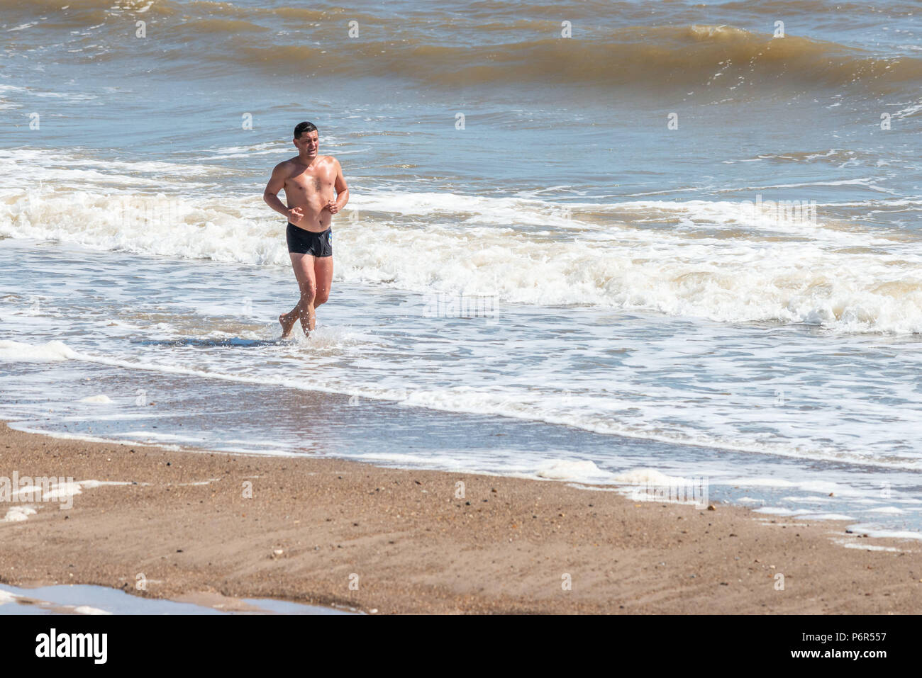 Skegness, UK, 2nd July 2018. A man jogging on the beach uses the incoming waves to keep himself cool, as the continued hot weather keeps temperatures in the UK at a high. Credit: Steven Booth/Alamy Live News. Stock Photo