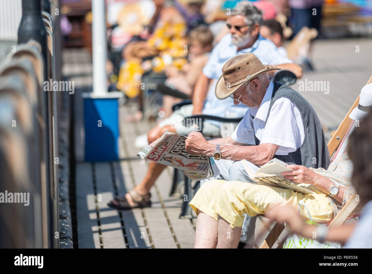 Skegness, UK. 2nd July 2018. As temperatures continue to rise across the UK during the current heatwave, an old man sits in his dekchair on Skegness Pier and reads his newspaper in the hot sunshine. Credit: Steven Booth/Alamy Live News. Stock Photo