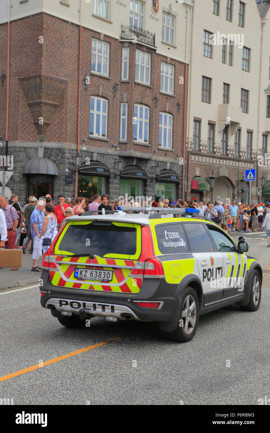 A crowd of people stand on the sidewalk while a dog patrol (canine unit) police vehicle drives along Bryggen in Bergen city, Norway. Stock Photo
