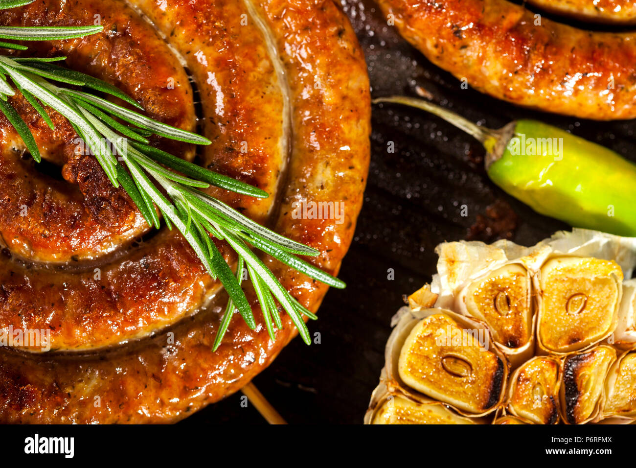 Closeup of grilled spiral sausages with vegetables and spices in a pan