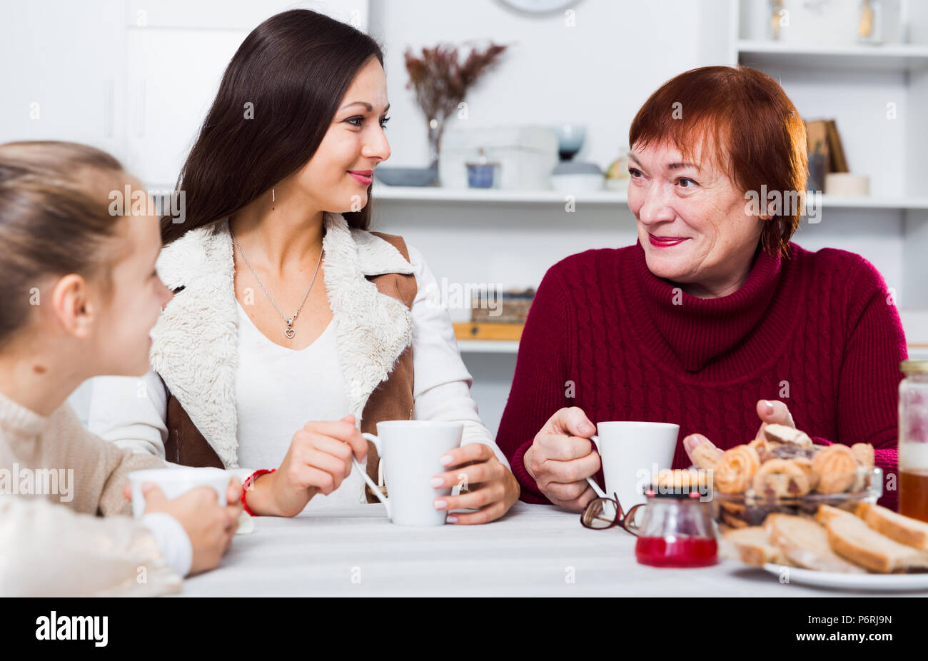 Three generations of happy family enjoying conversation over cup of ...