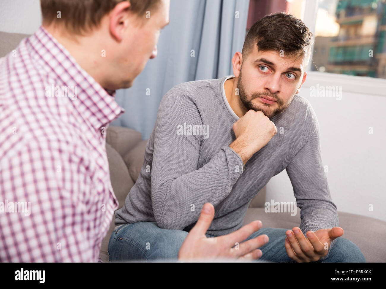 Upset man having unpleasant talk with male colleague on couch in home interior Stock Photo