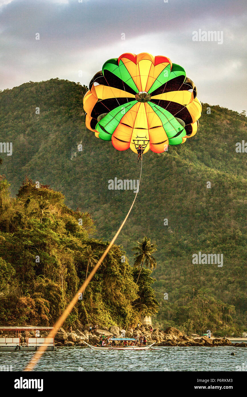 Parasailing over White Beach with tropical forested mountains in the background at Puerto Galera, Oriental Mindoro, Philippine Island Stock Photo