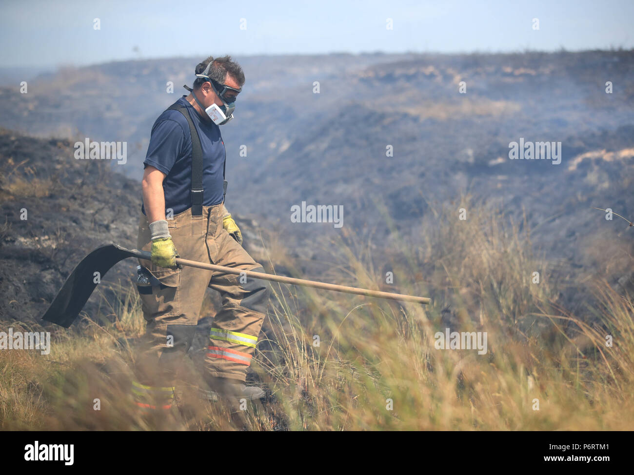 A firefighter from Tyne and Wear Fire and Rescue Service puts out the fire on Winter Hill near Bolton, as more than 20 fire engines are at the scene with crew tackling the moorland fires. Stock Photo