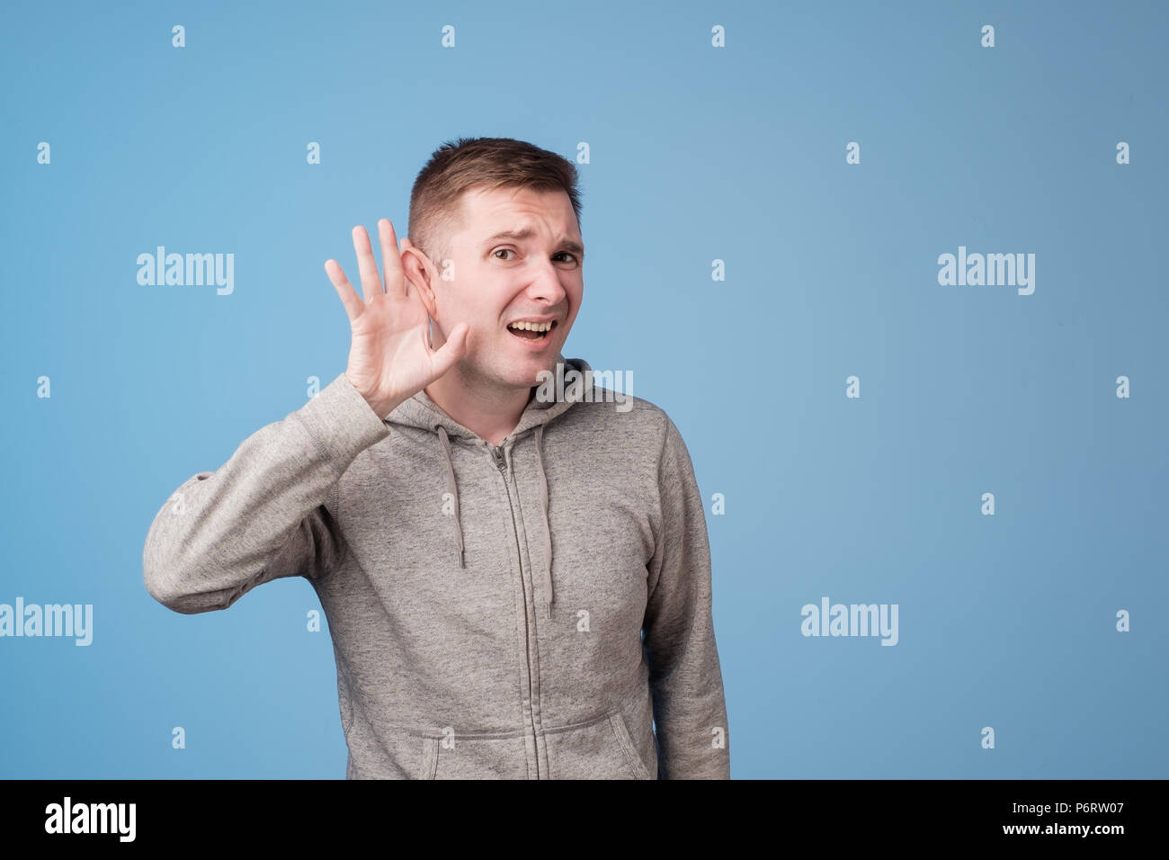 Closeup portrait of european man placing hand on ear listening carefully to gossip isolated on colored blue background Stock Photo