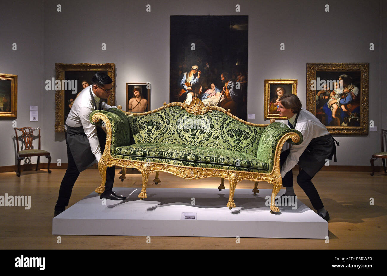 Gallery assistants adjust a George III Giltwood sofa, designed by Robert Adam and made by Thomas Chippendale, during a photocall for Christie's classic week sales, in London. Stock Photo