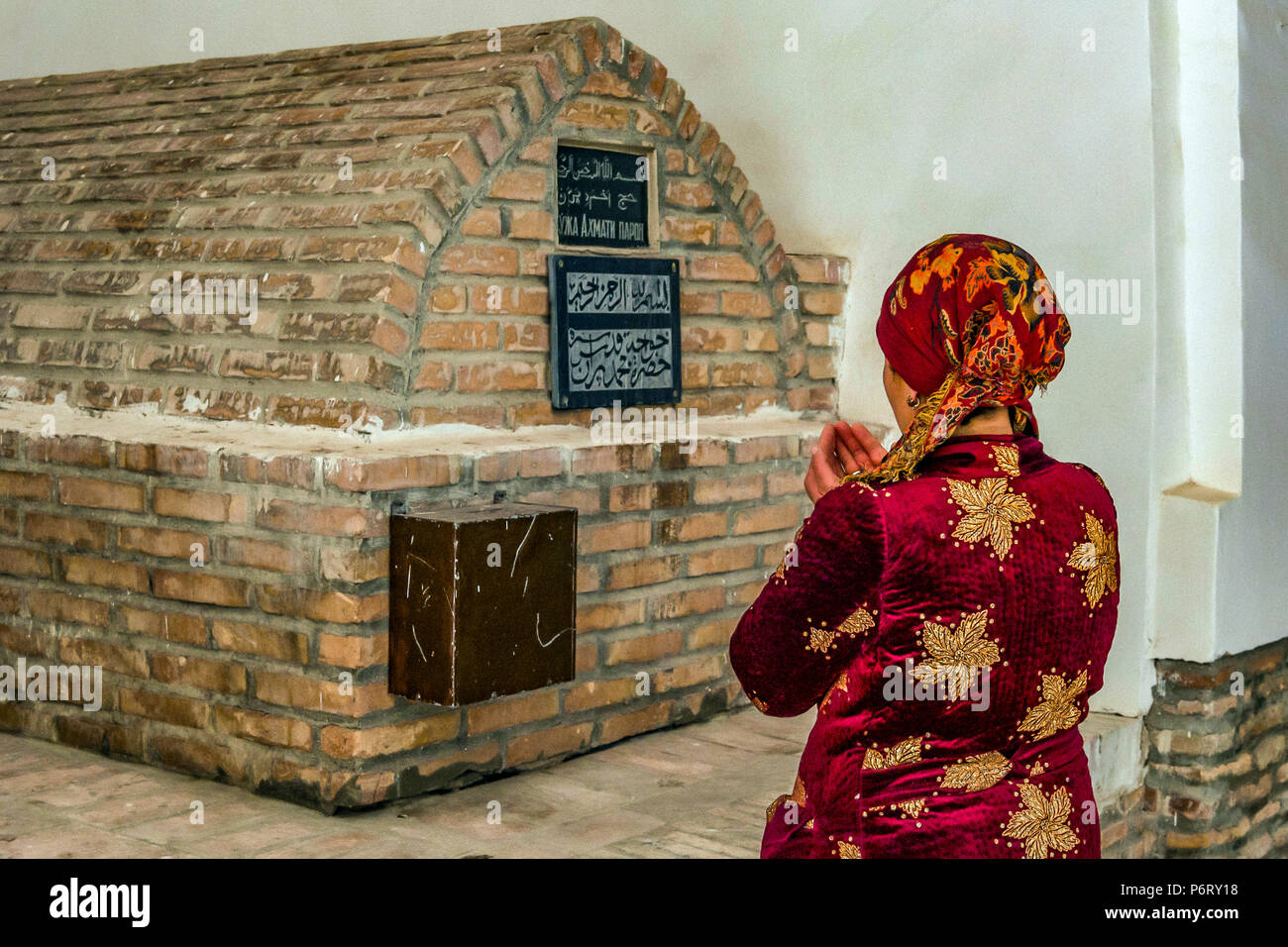 A woman prays to a tomb inside the Bazar Taki-Telpak Furushon, in Bukhara, Uzbekistan Stock Photo