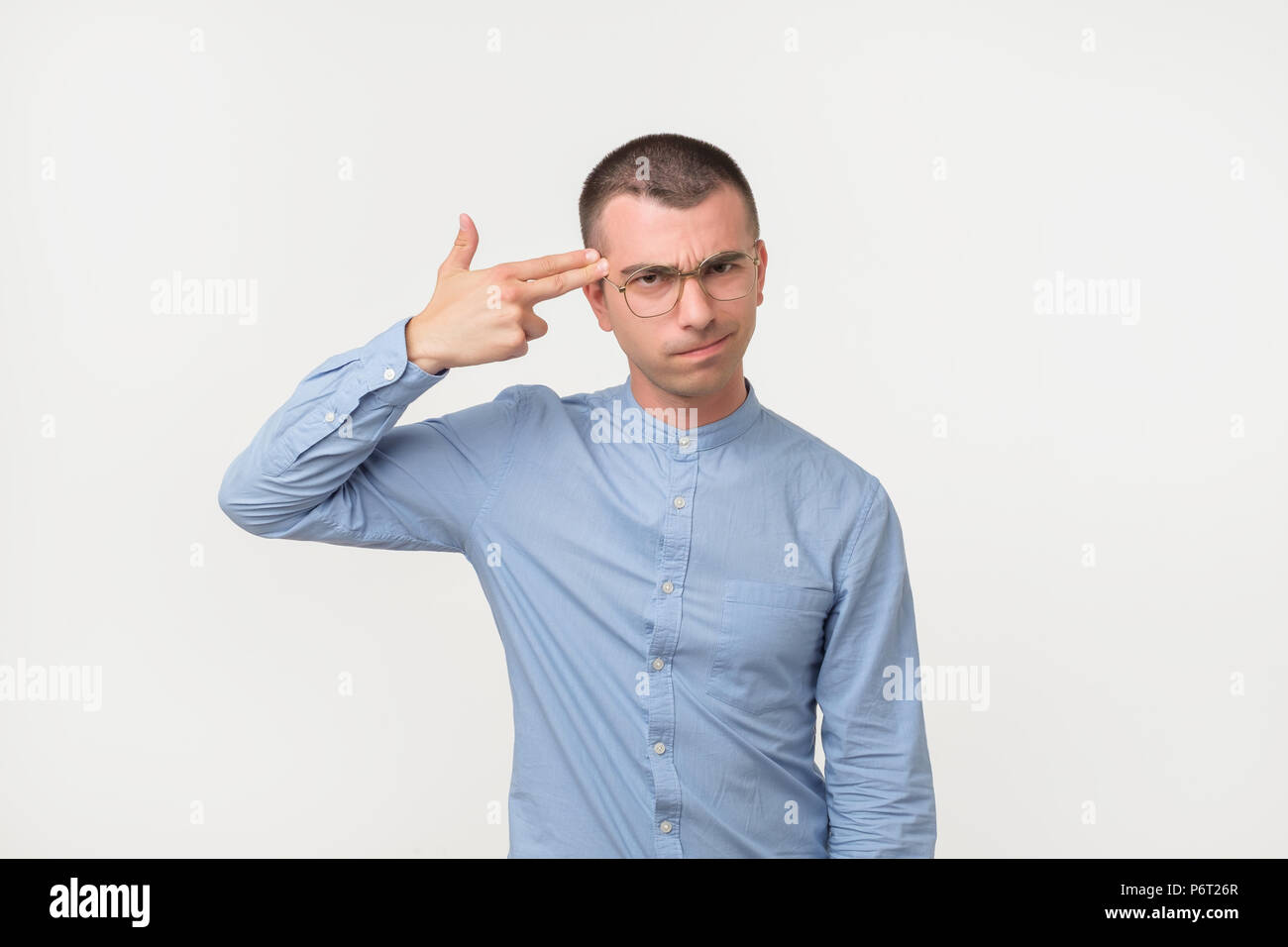 Tired or bored hispanic guy holding gun gesture near temples and making faces while standing over gray background. Stock Photo