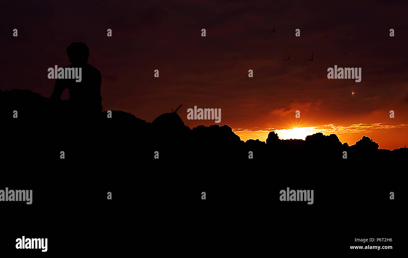 Silhouette young man sitting on top of a mountain with beautiful sunset ...