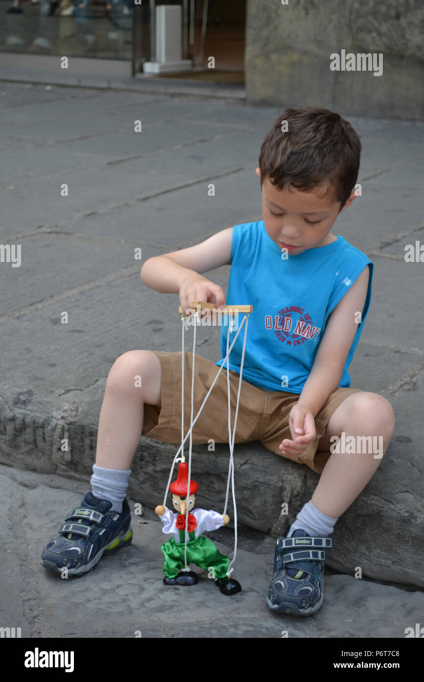 A young boy sitting on the pavement in Florence, Italy, plays with a Pinocchio puppet Stock Photo