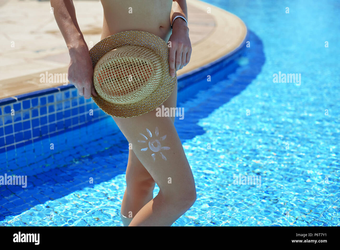 Sunscreen and beautiful female feet in the summer pool, the concept of protecting the skin Stock Photo