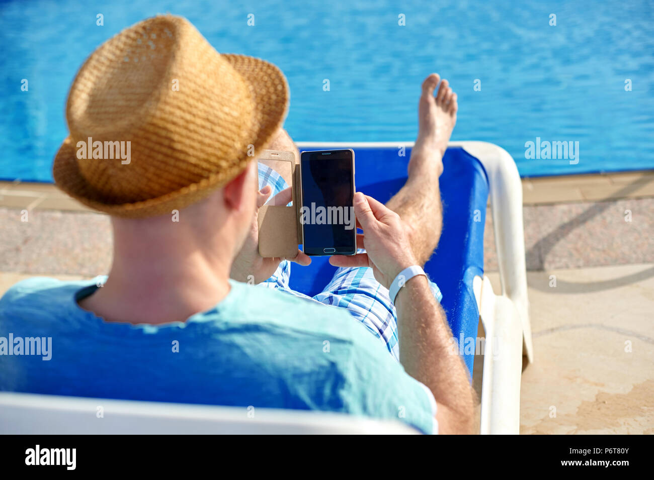 Man using mobile phone on vacation by the pool in hotel, concept of a freelancer working for himself on vacation and travel Stock Photo