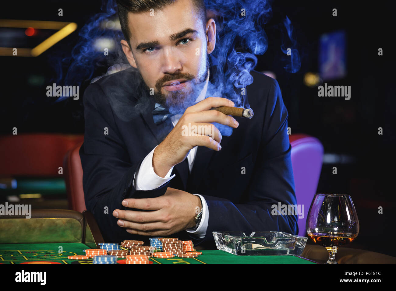 Rich handsome welldressed man smoking cigar and playing roulette in