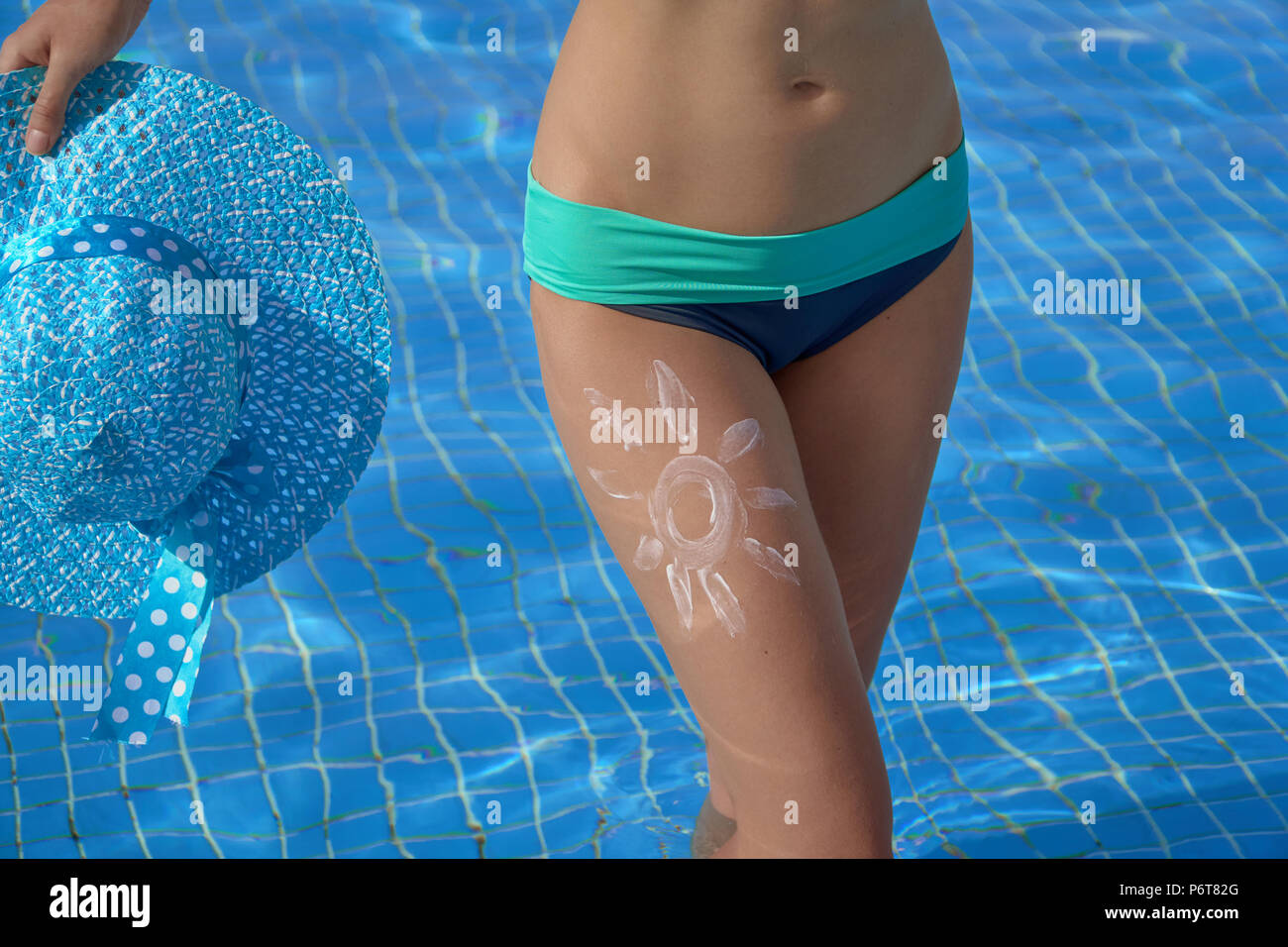 Sunscreen and beautiful female feet in the summer pool, the concept of protecting the skin Stock Photo