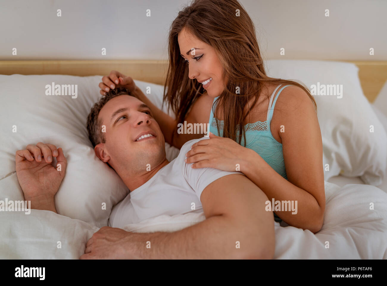 Beautiful young woman waking up her cute smiling man in bed in the morning. Stock Photo