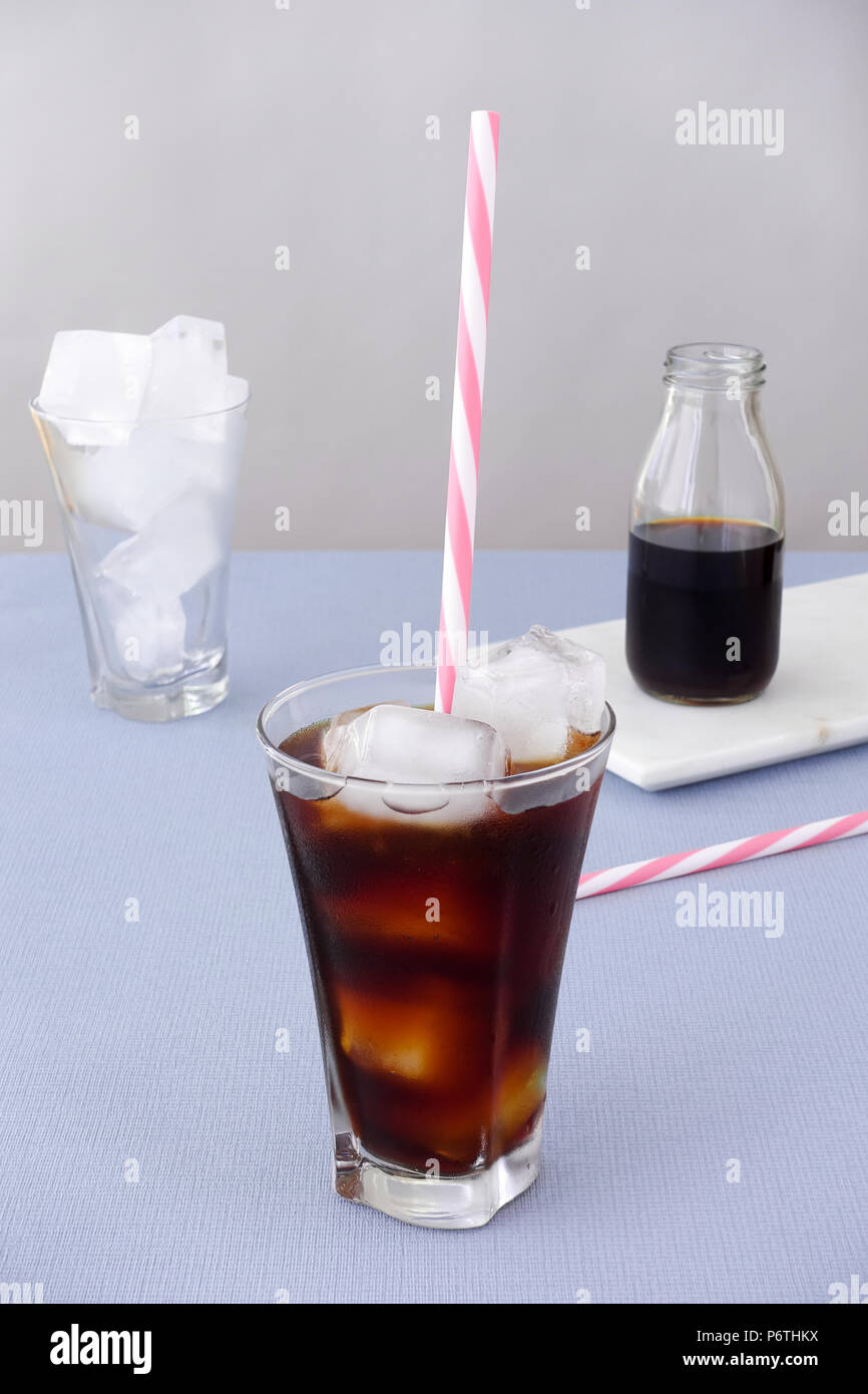 Ice coffee in a glass with ice cubes and straw on violet background and a bottle of cold brew coffee concentrate on white marble board. High angled vi Stock Photo