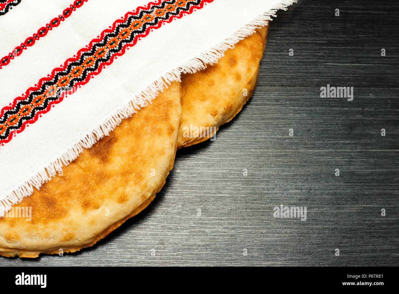 Two fresh pita bread under multicolor napkin. Wooden texture. Rustic food background. Top view. Copy space Stock Photo