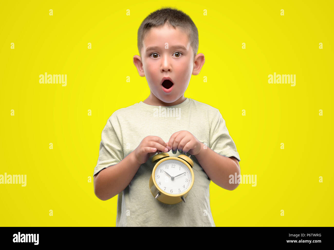Little child holding alarm clock scared in shock with a surprise face