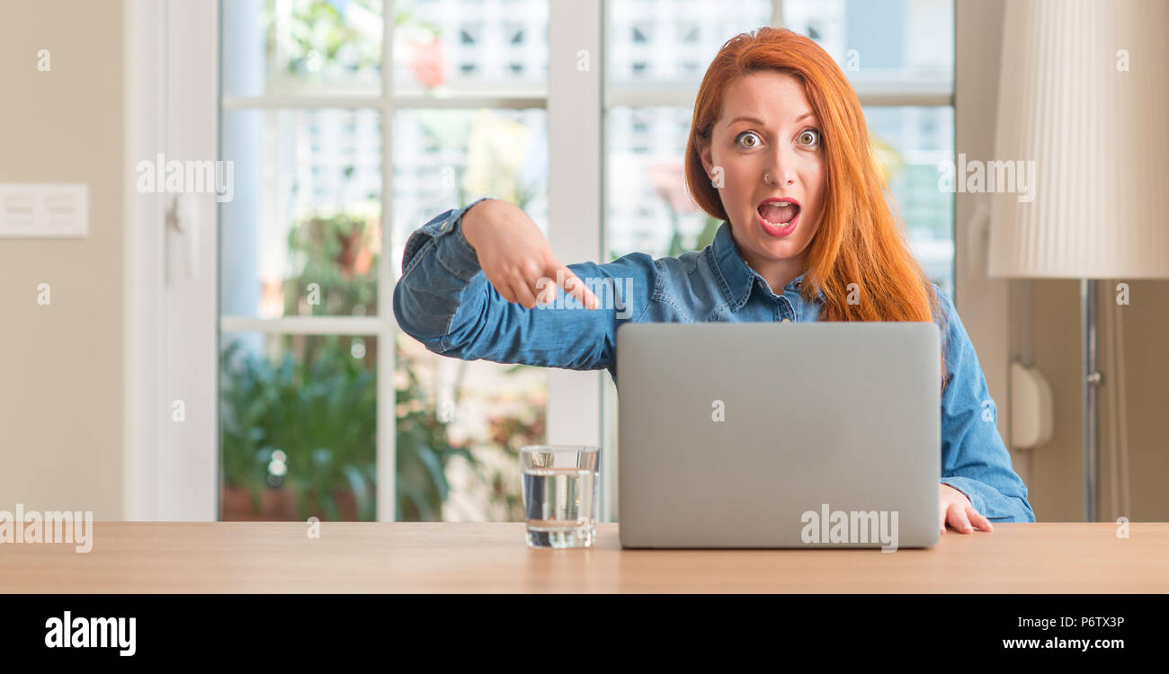 Redhead woman using computer laptop at home very happy pointing with ...