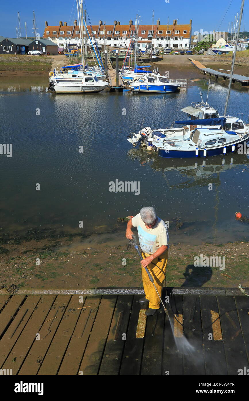 Fisherman cleaning wooden dock with water pipe at Axe Yacht Club in Seaton, Devon Stock Photo