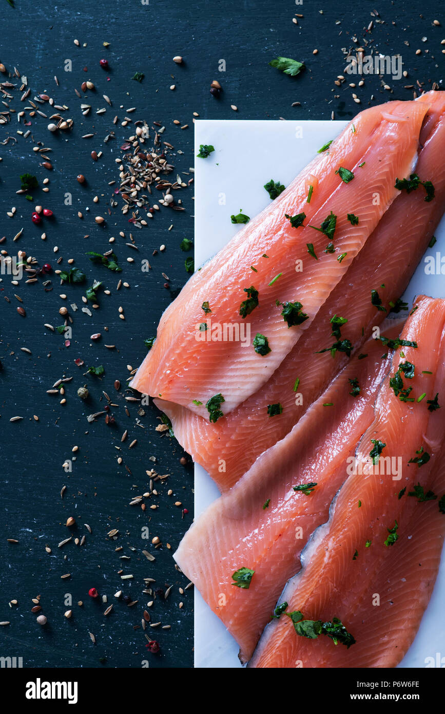 high angle view of some slices of raw trout on a white marble tray, on a dark rustic surface sprinkled with herbs and spices Stock Photo