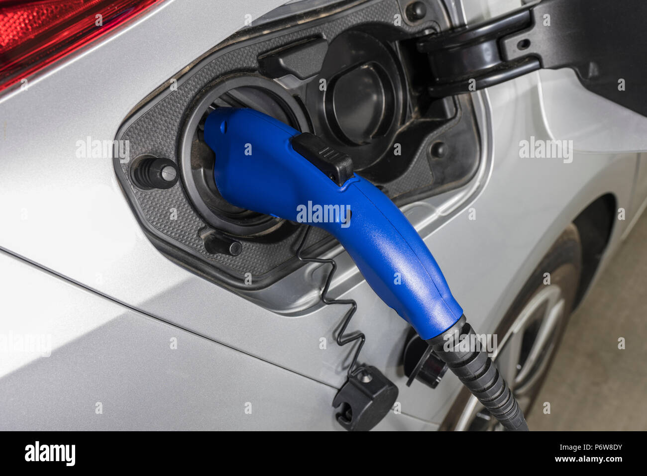 Close up of electric vehicle plug charging car inside garage. Stock Photo