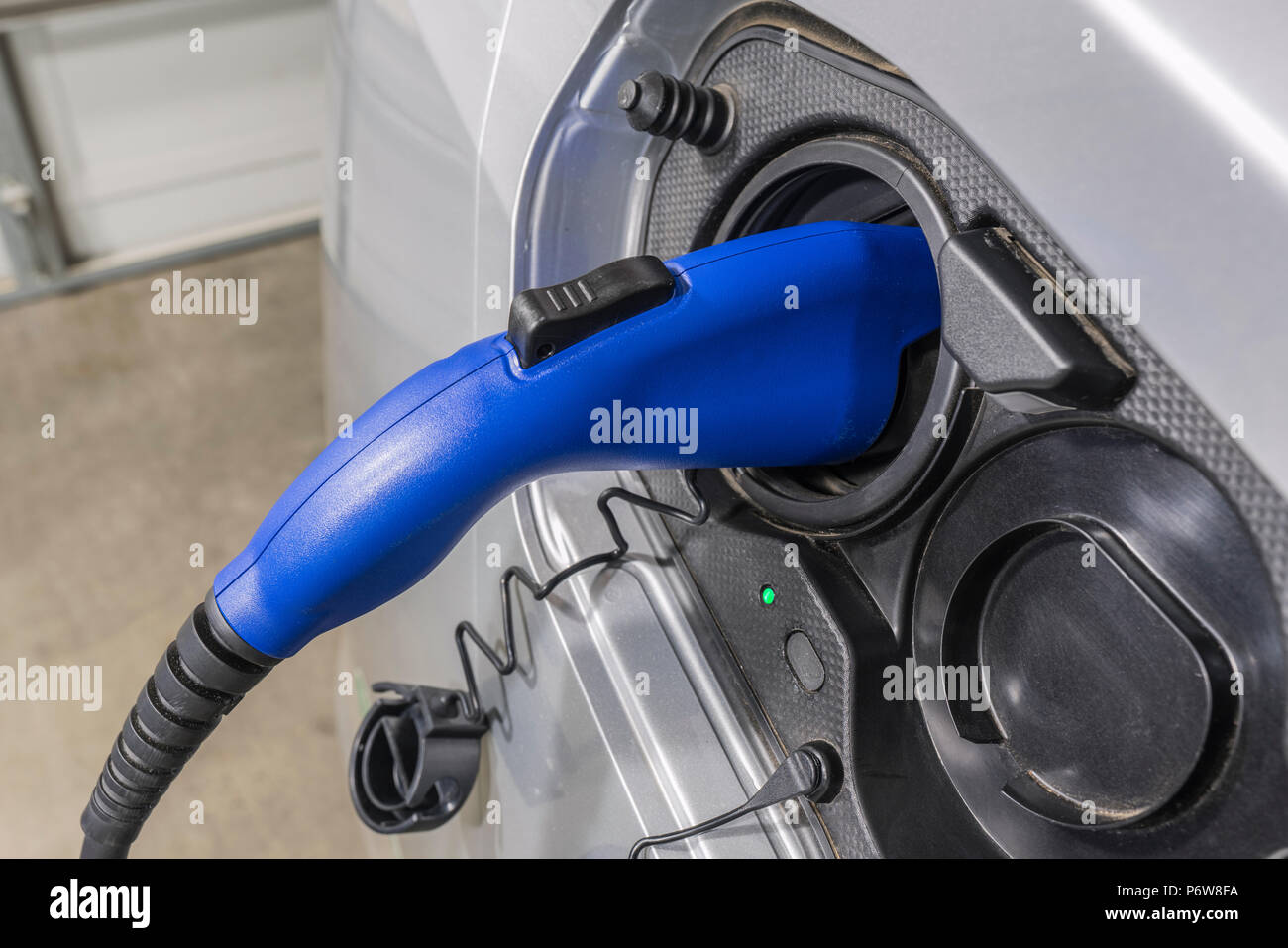 Close up of electric vehicle plug charging car inside a residential garage. Stock Photo