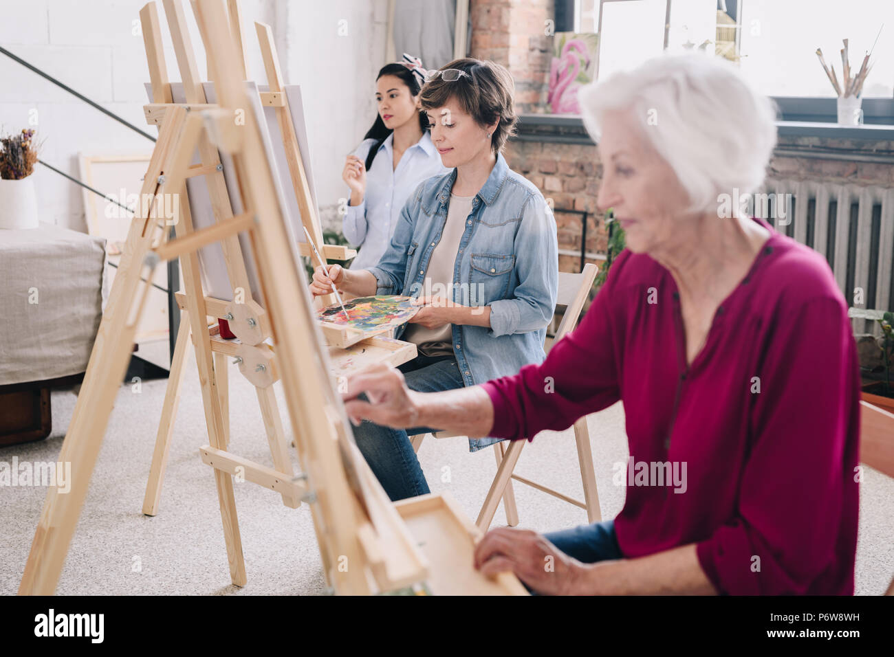 Portrait of art students sitting in row and painting at easels in art  studio, focus on smiling adult woman enjoying work in center, copy space  Stock Photo - Alamy