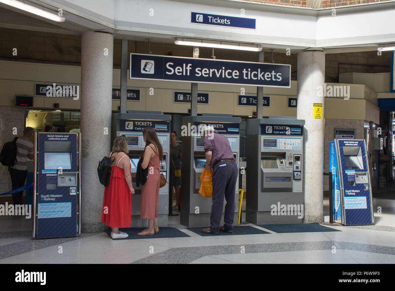 Train passengers buying tickets from self service machines inside the ticket office at Guildford railway station, Surrey, UK Stock Photo