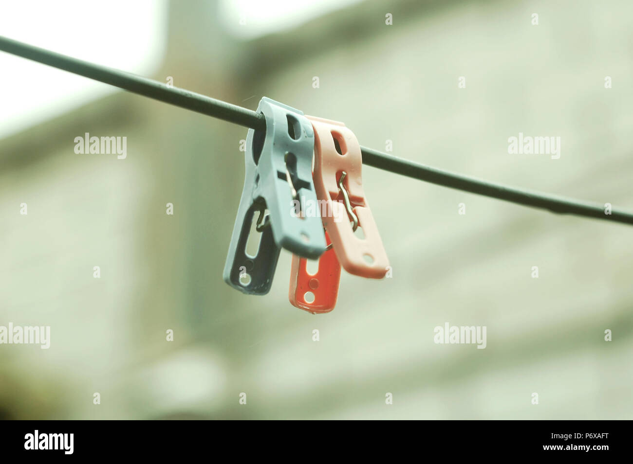 Two plastic clothespins on a rope on the background of a brick wall of house. Selective focus, cloudy day. Stock Photo