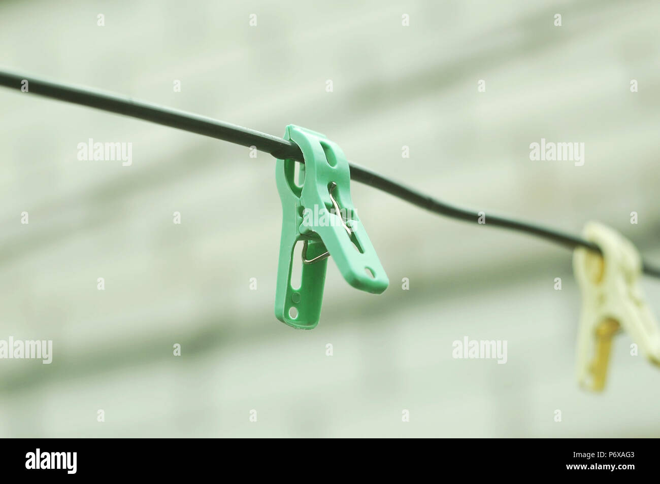 Two clothespins on a rope on the background of a brick wall of house. Selective focus, cloudy day. Stock Photo