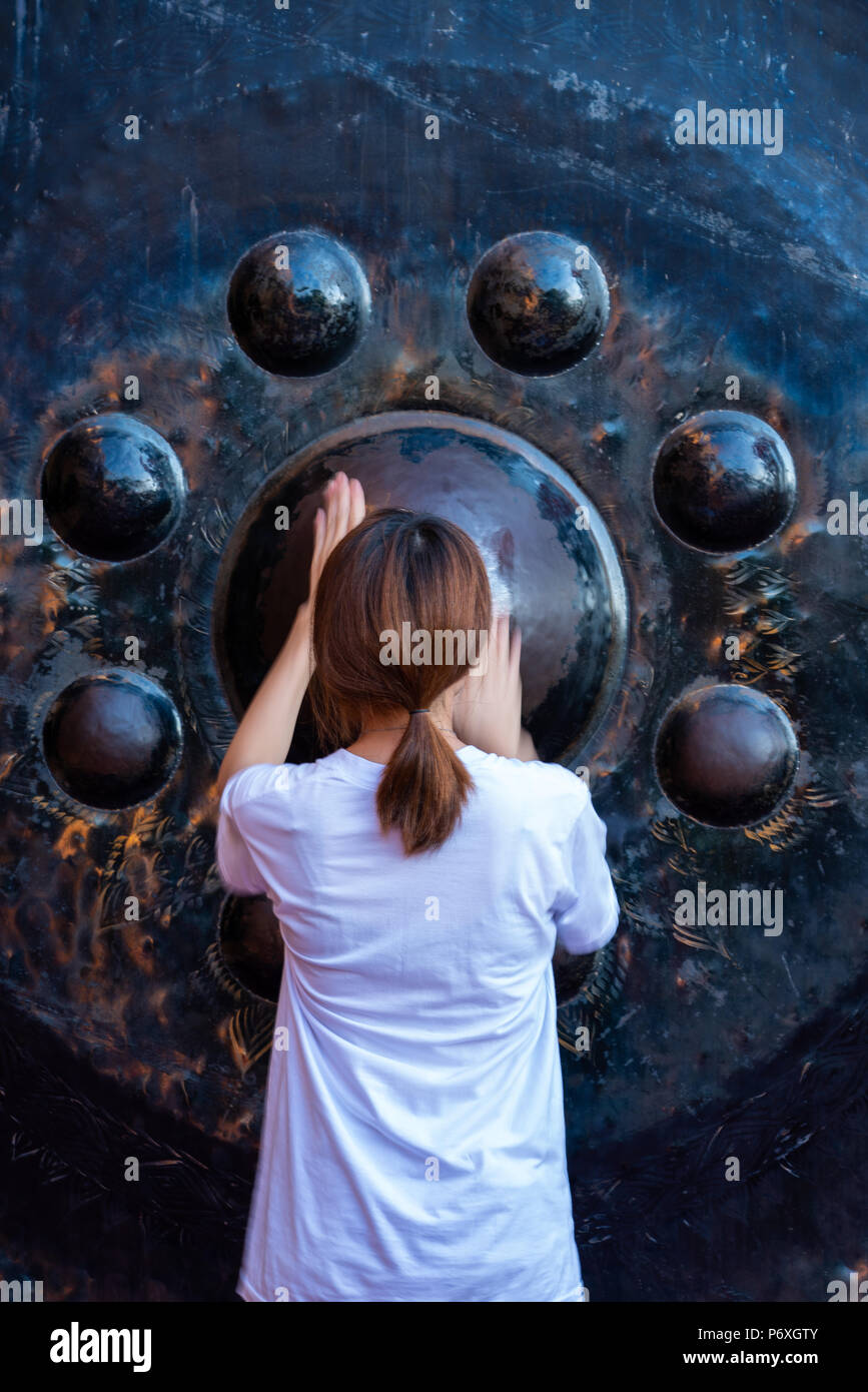 Kanchanaburi, Thailand - May 13, 2018: White shirt woman tourist rubbing large black gong in Buddhist temple wishing blessing from Buddha in Tham Sua  Stock Photo