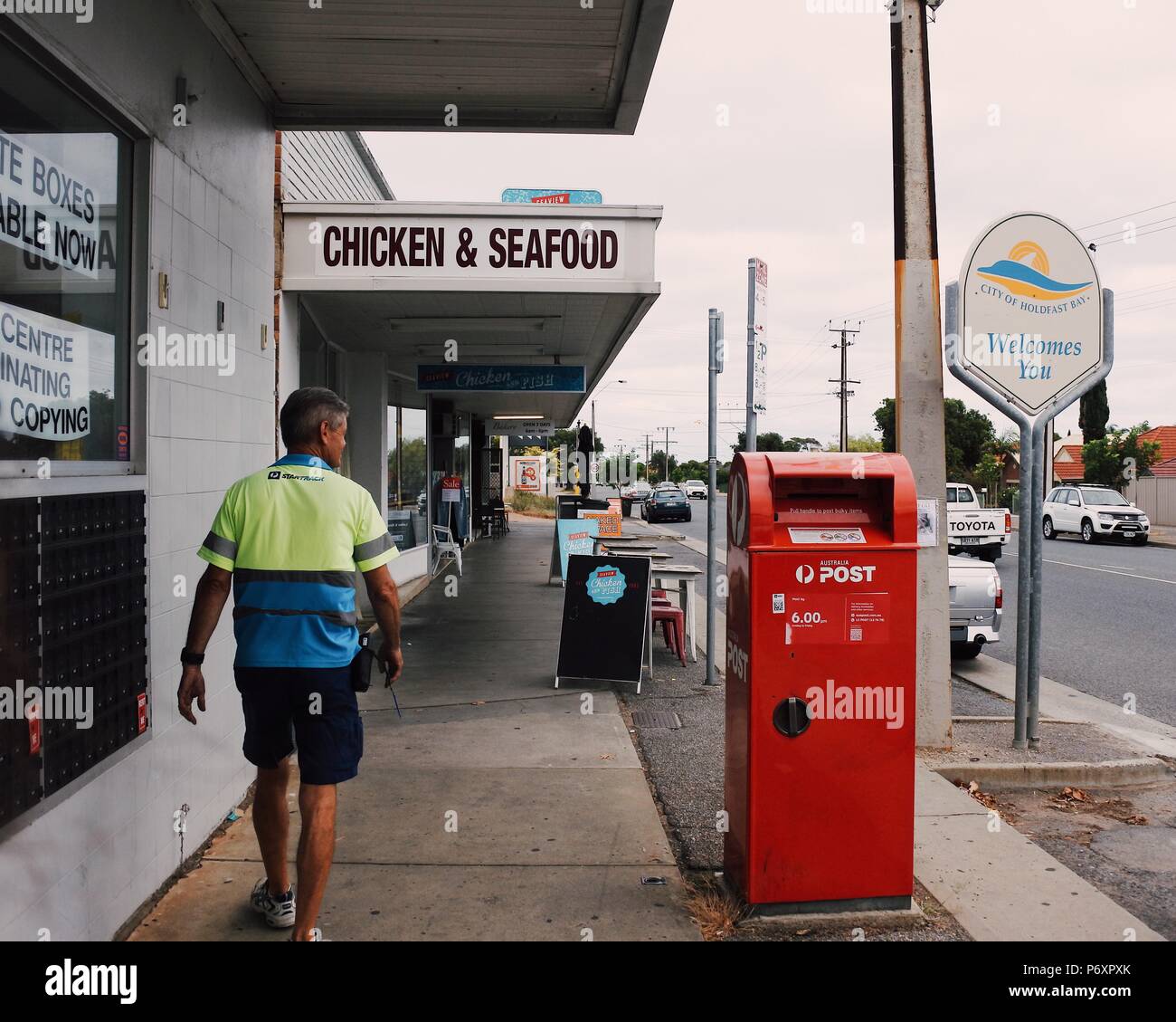 Post office and postman with fish and chips shop in the background at street in Seaview Downs, Adelaide Stock Photo