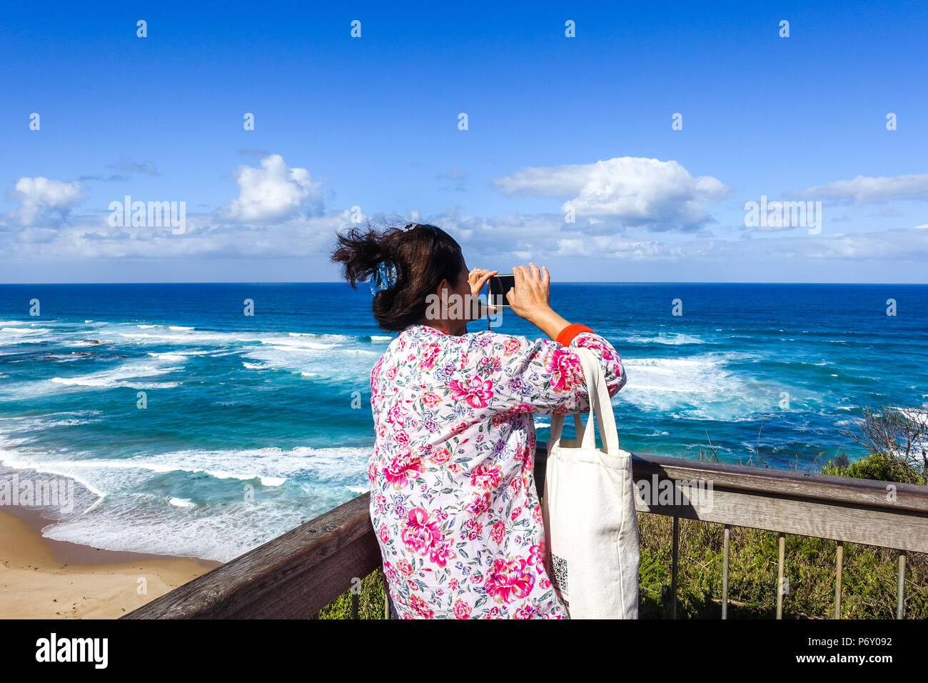 Chinese middle-age female tourist taking photos with mobile phone at Castle Cove Lookout on Great Ocean Road, VIC Australia. Stock Photo