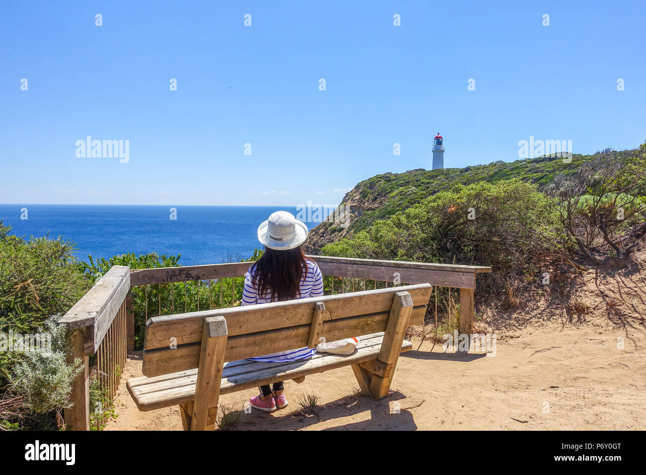 Female tourist sitting on viewing platform overlooking beautiful ocean view and lighthouse at Cape Schanck. Mornington Peninsula, VIC Australia. Stock Photo